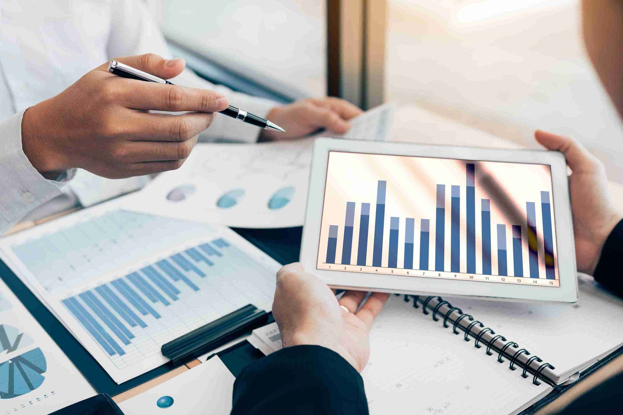 Business professionals analyzing graphs on a tablet during a meeting, focused on data-driven decision-making.