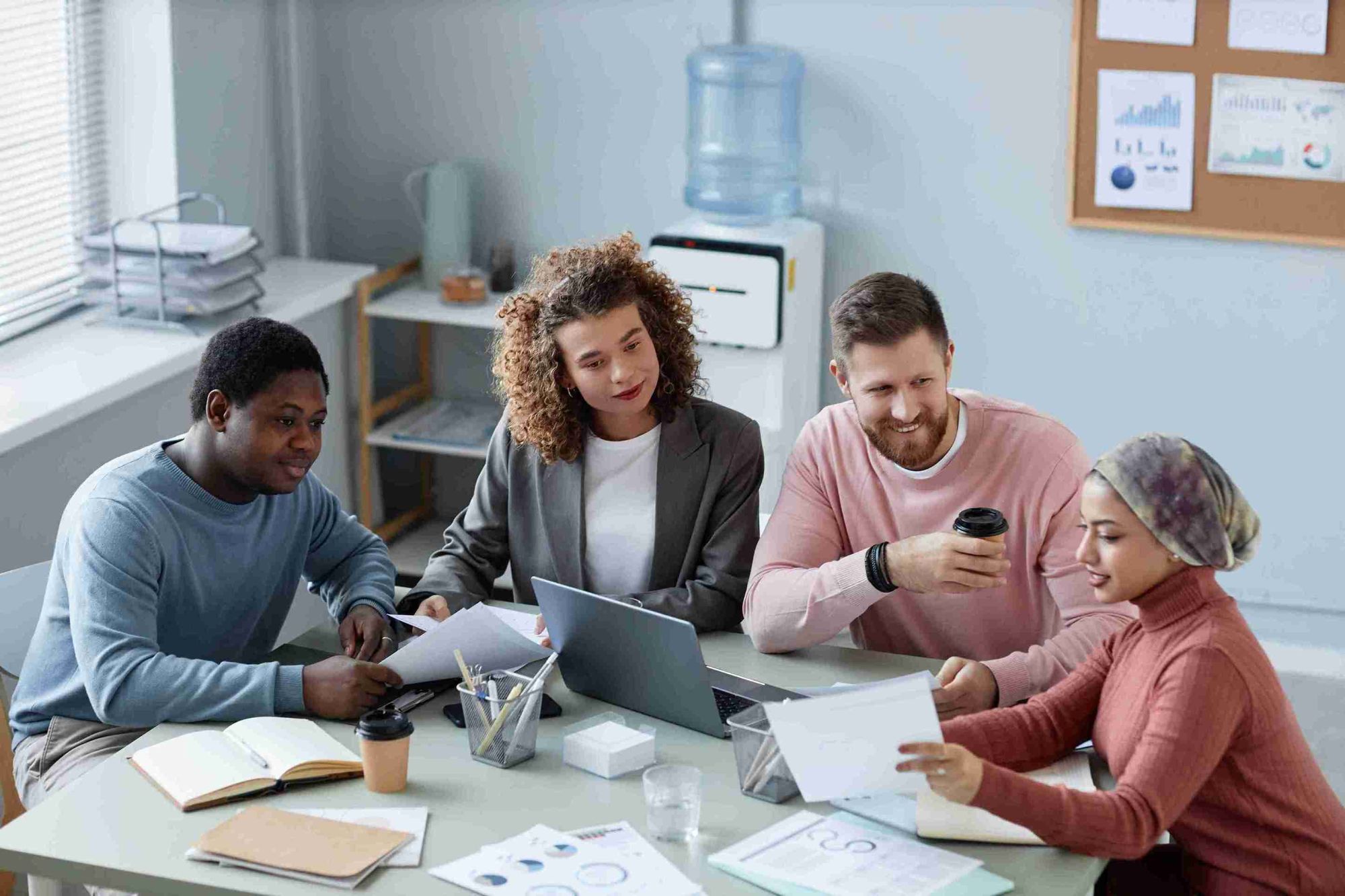 A diverse group of people collaborating around a table, each using laptops for a productive discussion
