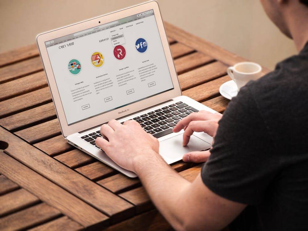 A man works on a laptop, focused, sitting at a wooden table in a cozy, well-lit environment.