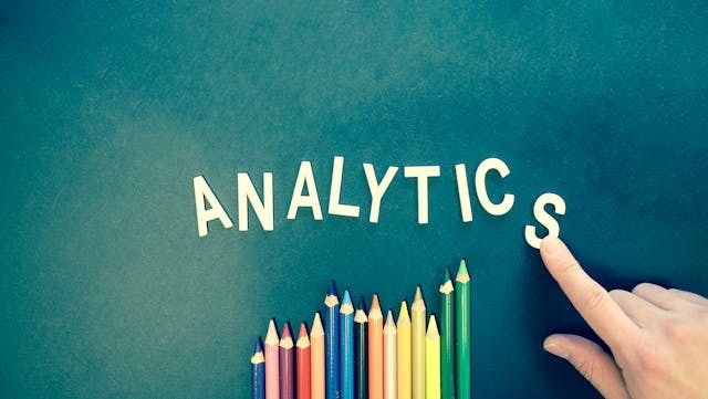 Analytics written on a blackboard, surrounded by colorful pencils, symbolizing education and data analysis.