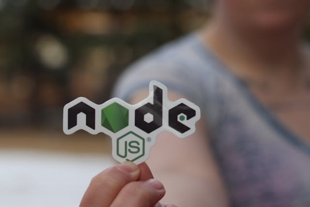 A person holds a sticker displaying the word "node," showcasing a vibrant design against a neutral background.