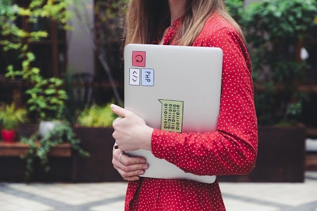 A woman confidently holds a laptop in her hand, ready to engage with technology.
