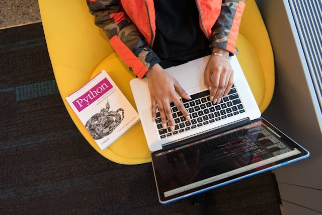 A person using a laptop while seated on a bright yellow chair, focused and engaged in their work