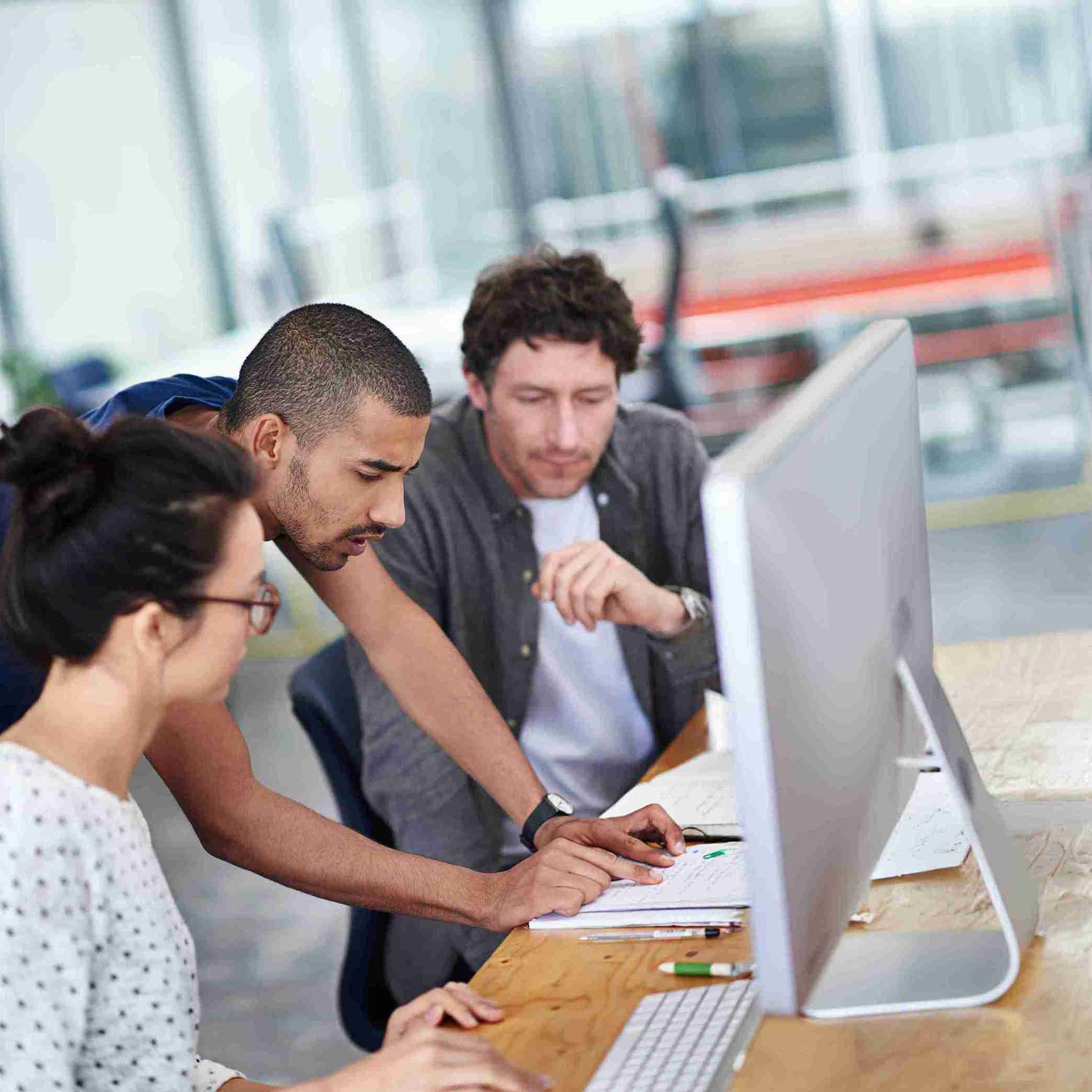 A diverse group of people collaborating around a computer, focused on their work and sharing ideas.