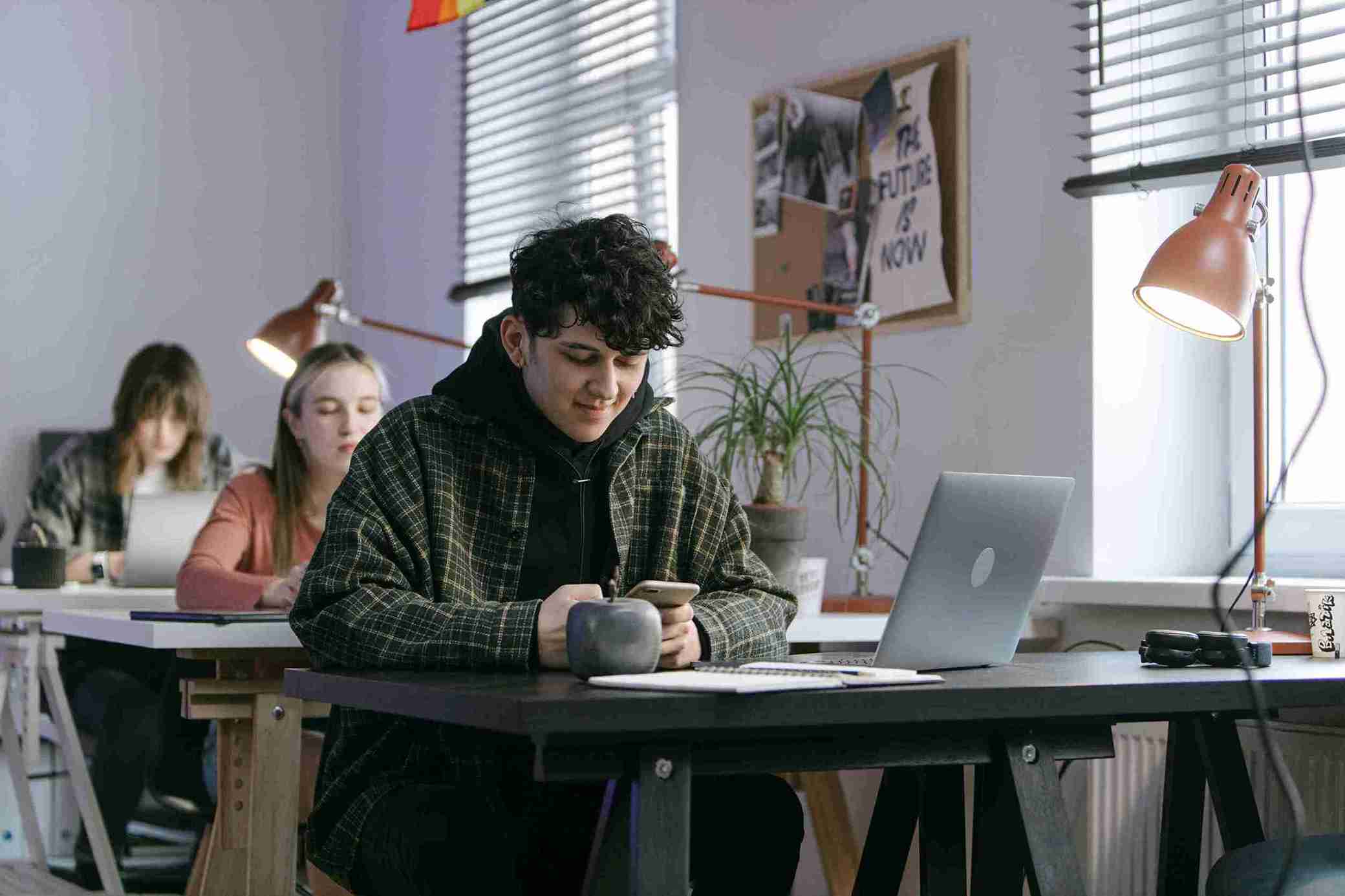 A man sits at a table, focused on his laptop, with a steaming cup beside him.