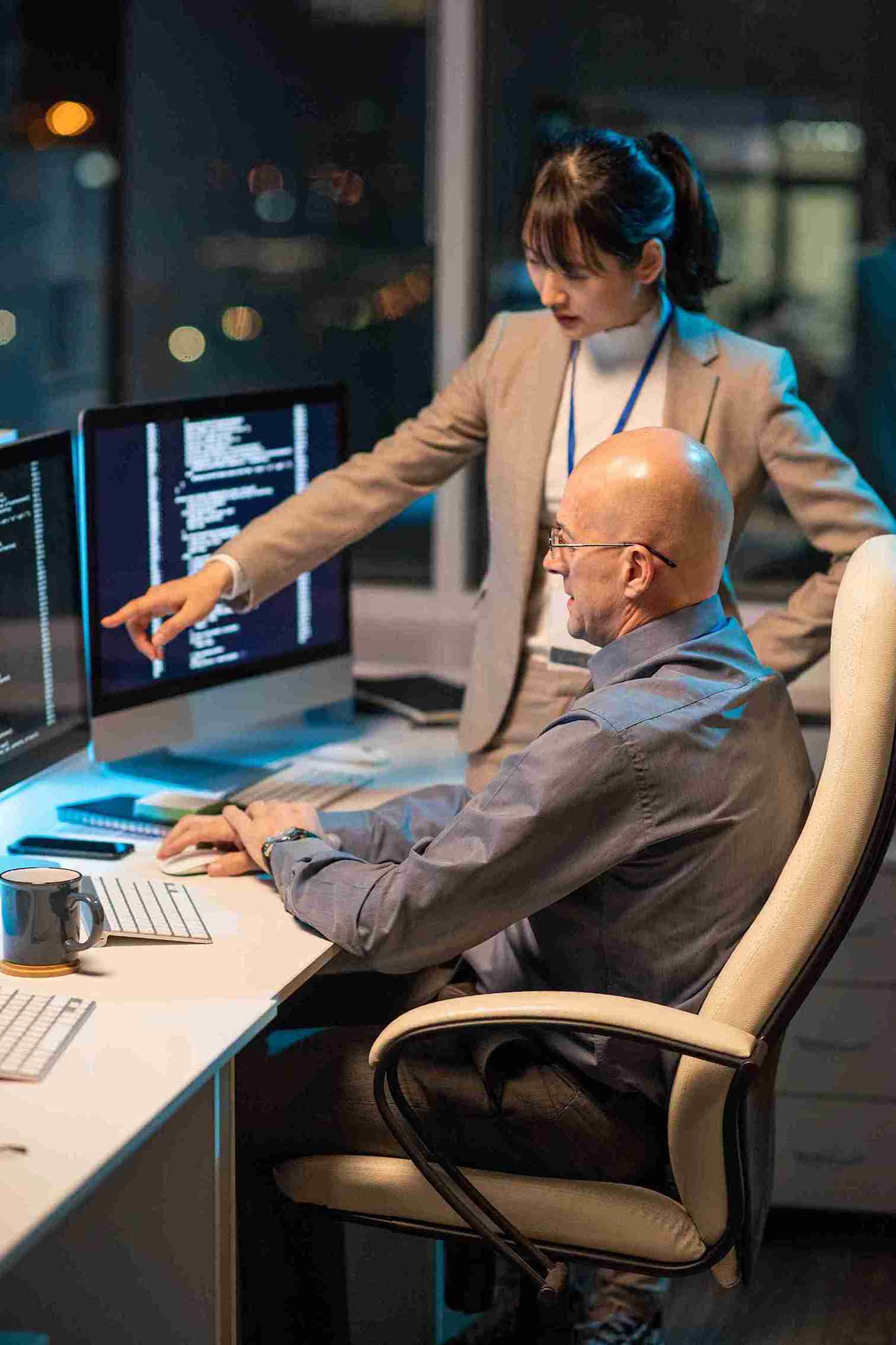young-asian-business woman-pointing Two people collaborating at computers in a modern office setting, focused on their work.